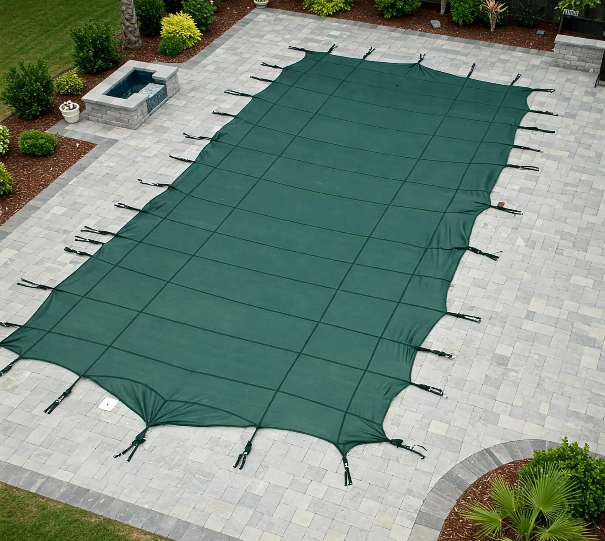 Swimming pool in Hugo, MN covered with a dark green, winter pool cover, securely fastened and extending slightly onto the surrounding paver deck.